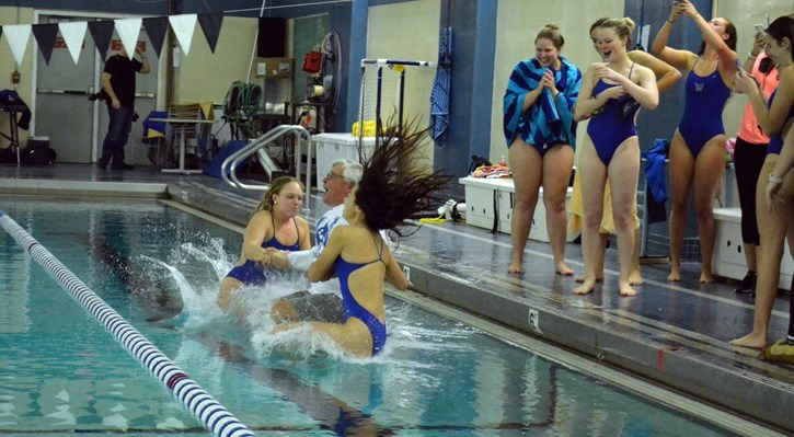 Owls captains Danielle MacDonald (l) and Tia Pariseau (r) toss coach Dave Laing into the pool to celebrate his 200th career coaching win during the 2017-18 season.
